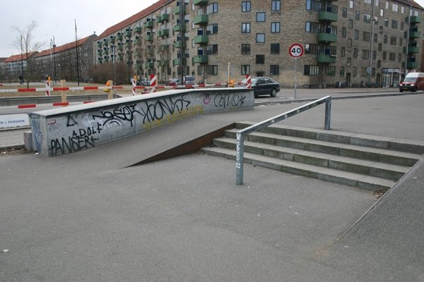 Nørrebro Skatepark is one of the most popular street parks in Copenhagen and offers a lot of challenges for the street oriented skater. The park is rectangular and provides a natural flow throughout the park with several obstacles along the way, including ledges, banks, rails and stairs.Nørrebro Skatepark is an exciting street park for skaters of all levels of experience. There are low ledges and fun banks for the beginners, however more experienced skaters can really take advantage of the park’s full potential. The asphalt foundation can seem hard for some skaters, however it can be used by skaters at all levels. The park has a well-developed course with things that you don’t see at many other parks. In addition, in 2013, the municipality of Copenhagen added a mini ramp which can both be used by beginners as well as experienced skaters who can use it to perfect their tricks.Every year, Nørrebro skatepark houses several competitions, for example Nørrebro Meltdown.Nørrebro Skatepark opened in 2007, and has been designed by Teit Andersen who is also the designer of Gentofte Skatepark. There has been made a few small changes to the park since then: A concrete bank at the corner of the park and a mini ramp.