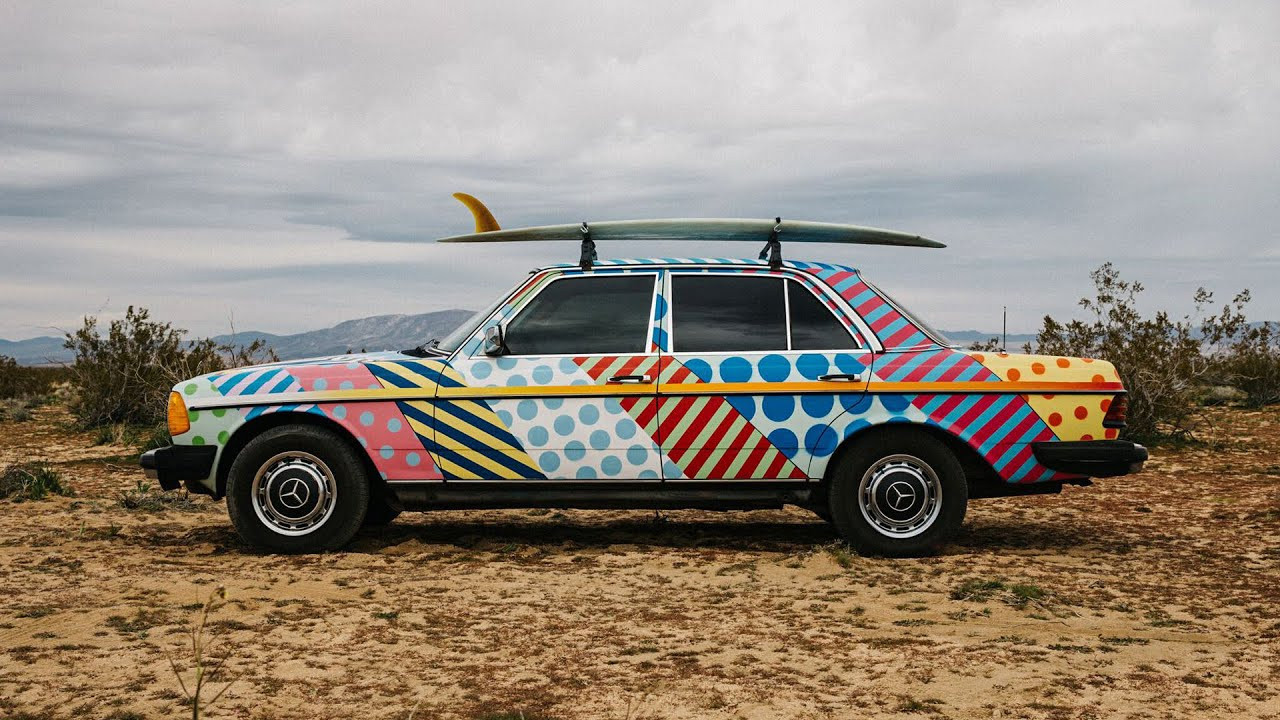Want to Win this Drivable Art Piece by Jason Woodside?<br /><br />This luxury sedan is called the "Cortex Cruiser" and it can be all yours.<br /><br />Throughout the decades, there's been an inextricable relationship between surfers and eccentric cars. This love affair is rooted in utility. In the ’50s, termite-infested woodies provided surfers both room and board—and room for their boards—on the cheap. Bondo-spotted Volkswagen buses became the standard issue of the ’60s. Eventually, any rust bucket with wheels that could get a surfer and their blade to some waves was used, abused and customized to better fit a surfy existence.<br /><br />SURFER Magazine has always been fond of these weird whips, especially ones with added flare. In the late ’50s, SURFER founder, John Severson, painted flower petals and waves all over his North Shore jalopy. The car's name, "Sunset Special", was tagged in one of his whimsical fonts across its doors. There's a picture of this car in SURFER's very first issue with a couple of D-finned logs popping out of its back window.<br /><br />In the late ’60s, SURFER's resident artist, Rick Griffin, painted psychedelic eyeballs getting barreled in cosmic lineups all over a beat-to-hell school bus. He then packed the bus full of shortboard revolutionaries and women and headed up California's coast in pursuit of fun waves and good times. You probably remember this scene from Severson's 1970 film, "Pacific Vibrations".<br /><br />Just when you thought the freewheeling days of surfers' wild-style cars were dead, white-washed by neutrally monotone Sprinter vans running into the six figures, an artist like James Woodside comes along and throws some color back on the scene. After scoring a 1982 Mercedes Benz 240d, Woodside blasted the luxury sedan with his artistic stylings and, like a cherry on top, slapped some surf racks on its roof. The "Cortex Cruiser" was born.<br /><br />SURFER recently caught up with Woodside to talk about the Cortex Cruiser, which he and our friends at Vissla are giving away. The Cortex Cruiser can be yours by clicking here: https://www.vissla.com/the-cortex-cruiser/